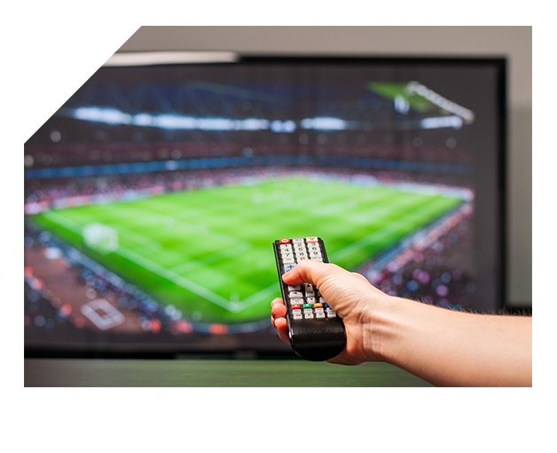 Main tenant une télécommande devant un écran diffusant un match de football en direct